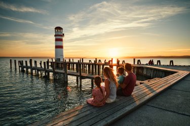 Familie sitzt bei Sonnenuntergang am Neusiedlersee mit Blick auf den Leuchtturm